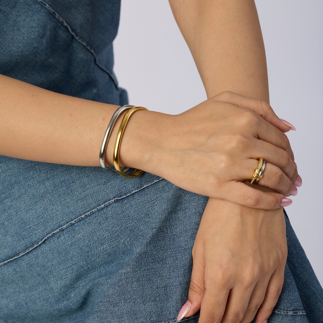 Close-up of a person's hands wearing gold bracelets and rings on a denim background