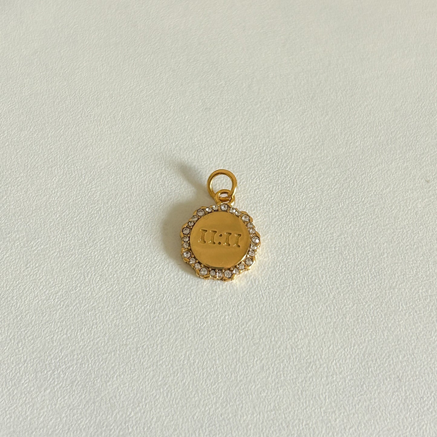 Gold 11:11 charm with engraved text on a light gray background
