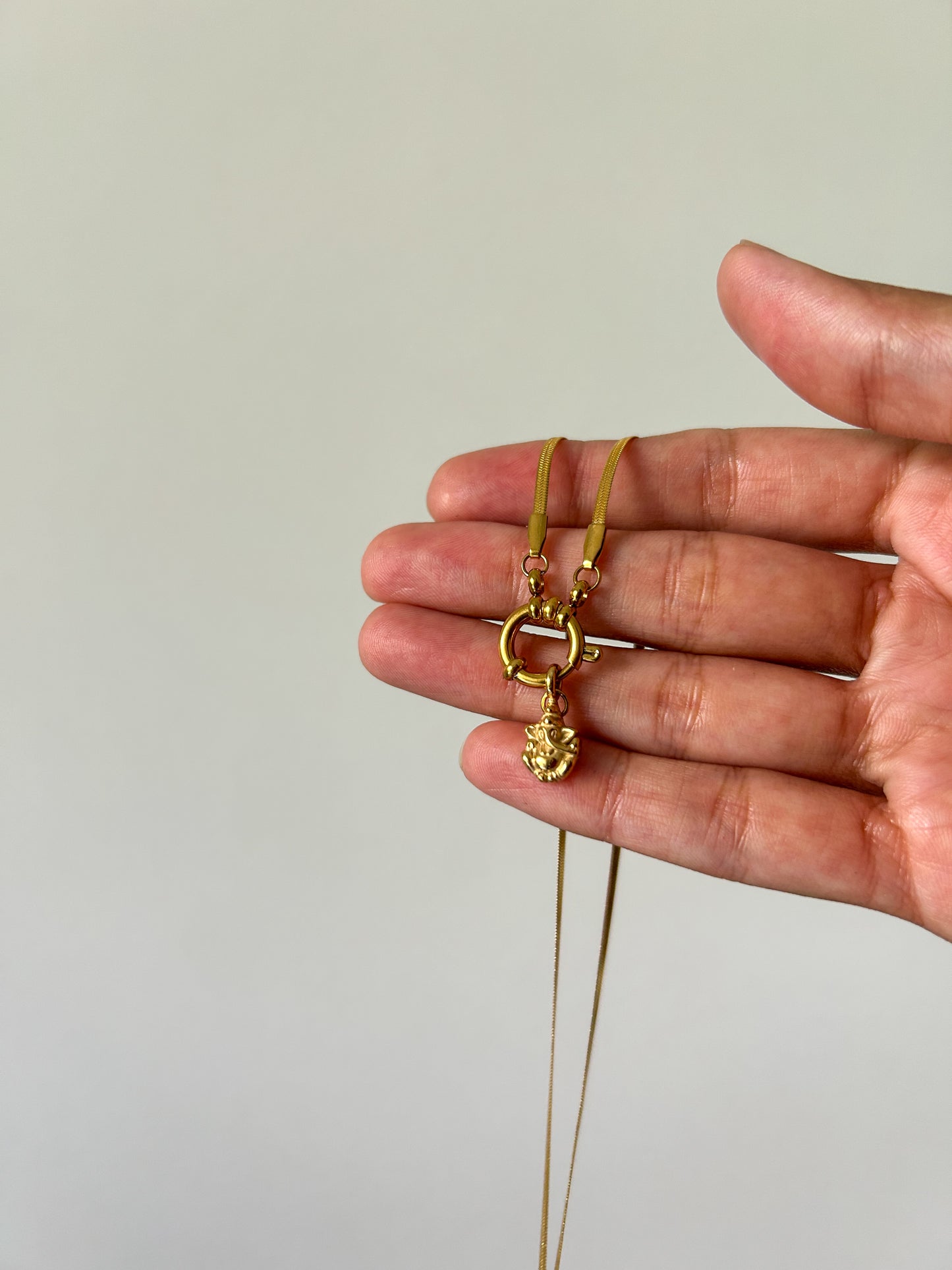 Gold necklace held in a hand against a plain background