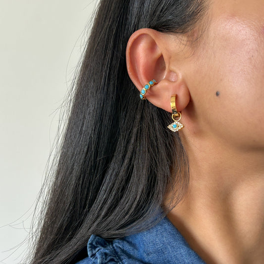 Close-up of a person wearing gold earrings with blue gemstones against a neutral background