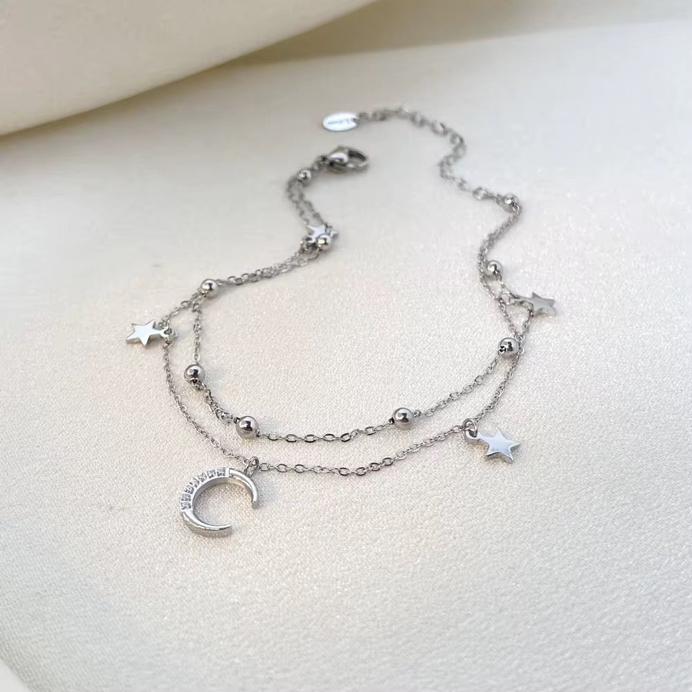 Silver anklet with star and moon charms on a light background