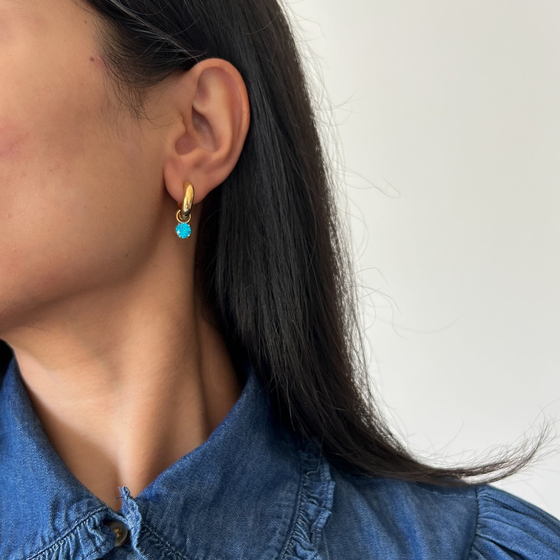 Close-up of a person wearing gold earrings with a blue gemstone against a white background