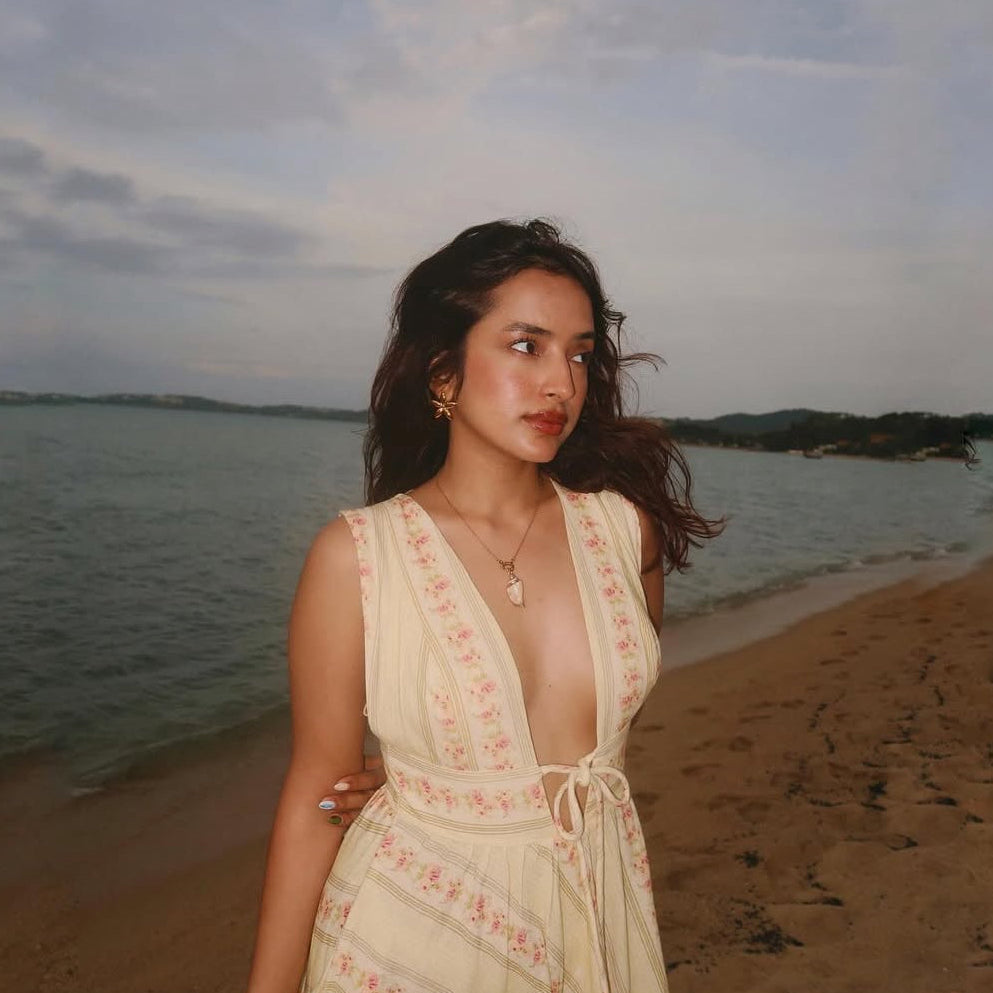 Woman in a sleeveless dress standing on a beach with water and sky in the background