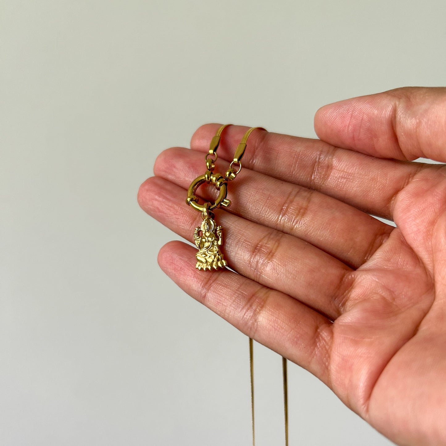 Gold necklace with a pendant held in a hand against a plain background