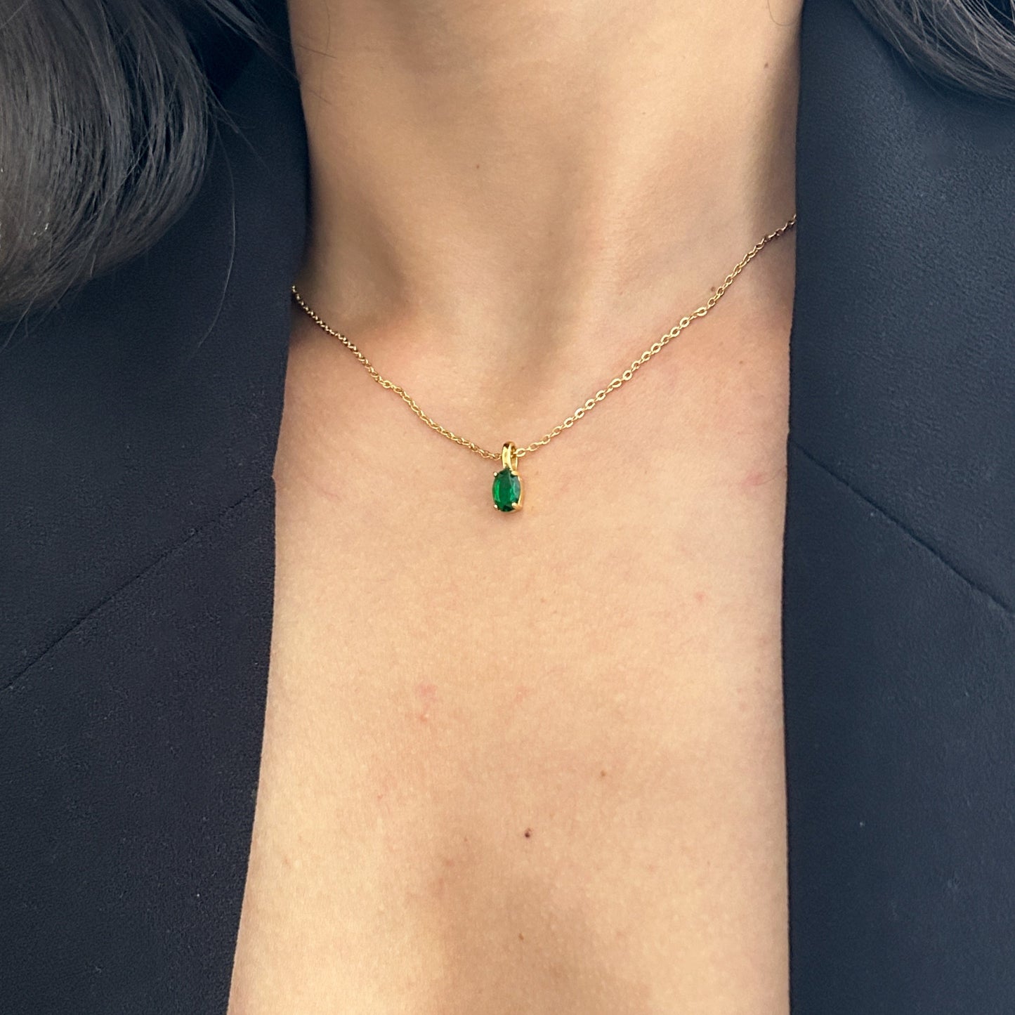 Gold necklace with a green gemstone pendant on a person's neck against a dark background