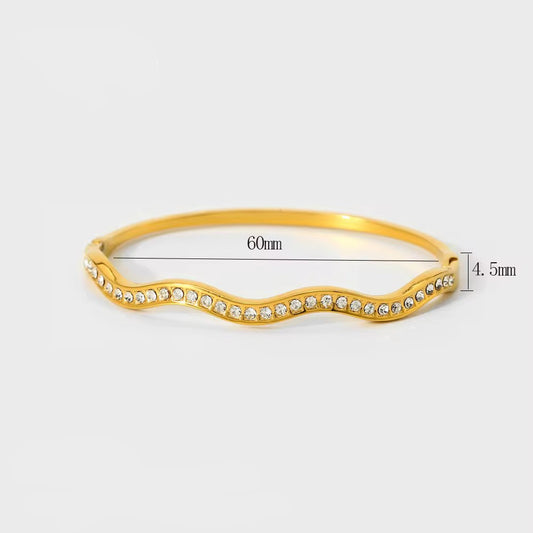 Gold bracelet with wavy design and embedded stones on a white background