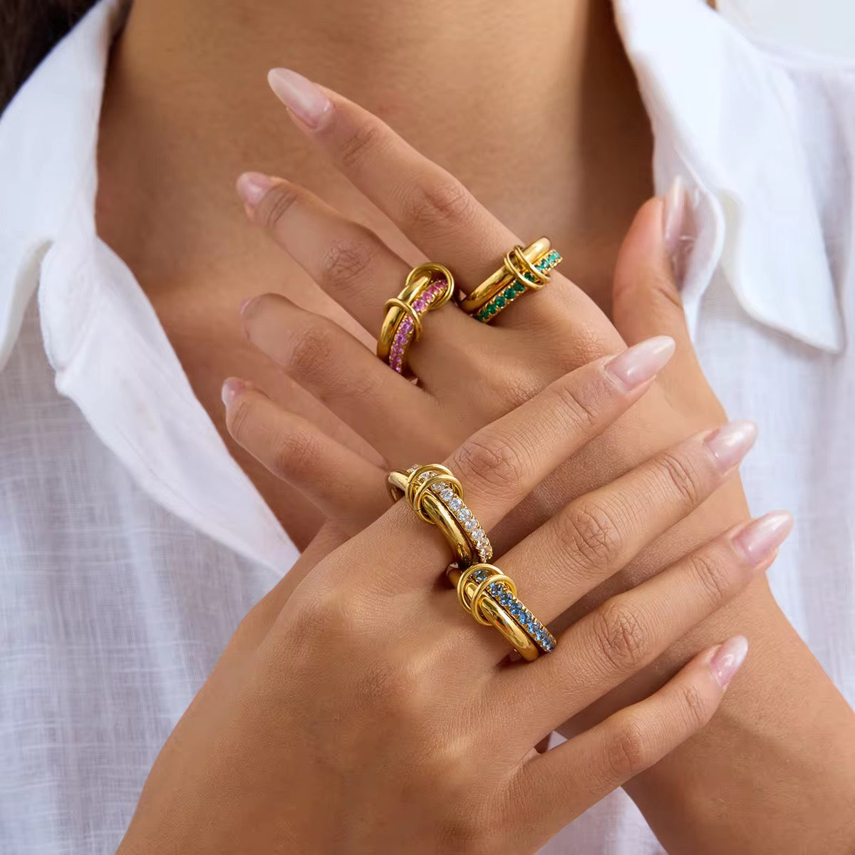 Close-up of a hand wearing multiple gold rings with gemstones against a white background