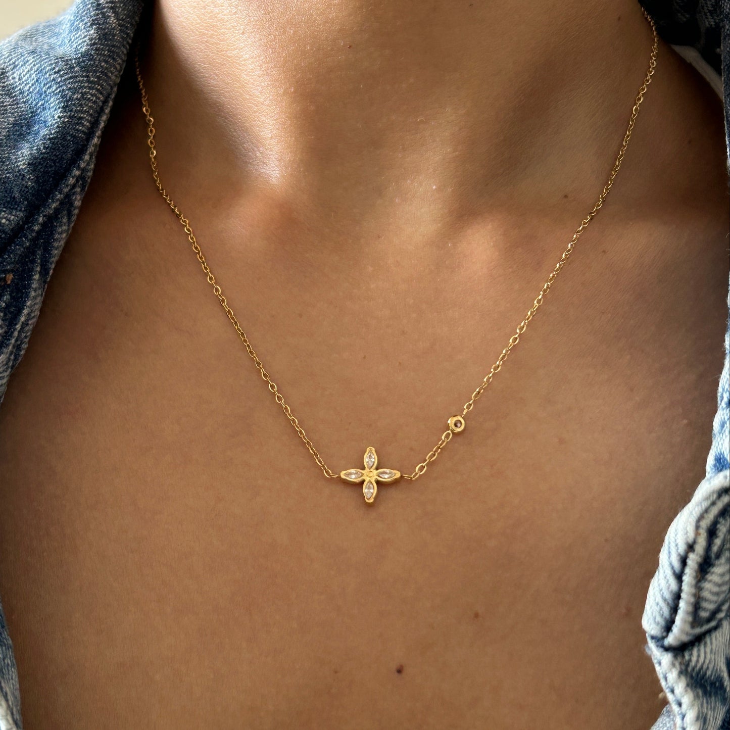 Gold necklace with a cross pendant on a person's neck, wearing a denim jacket.