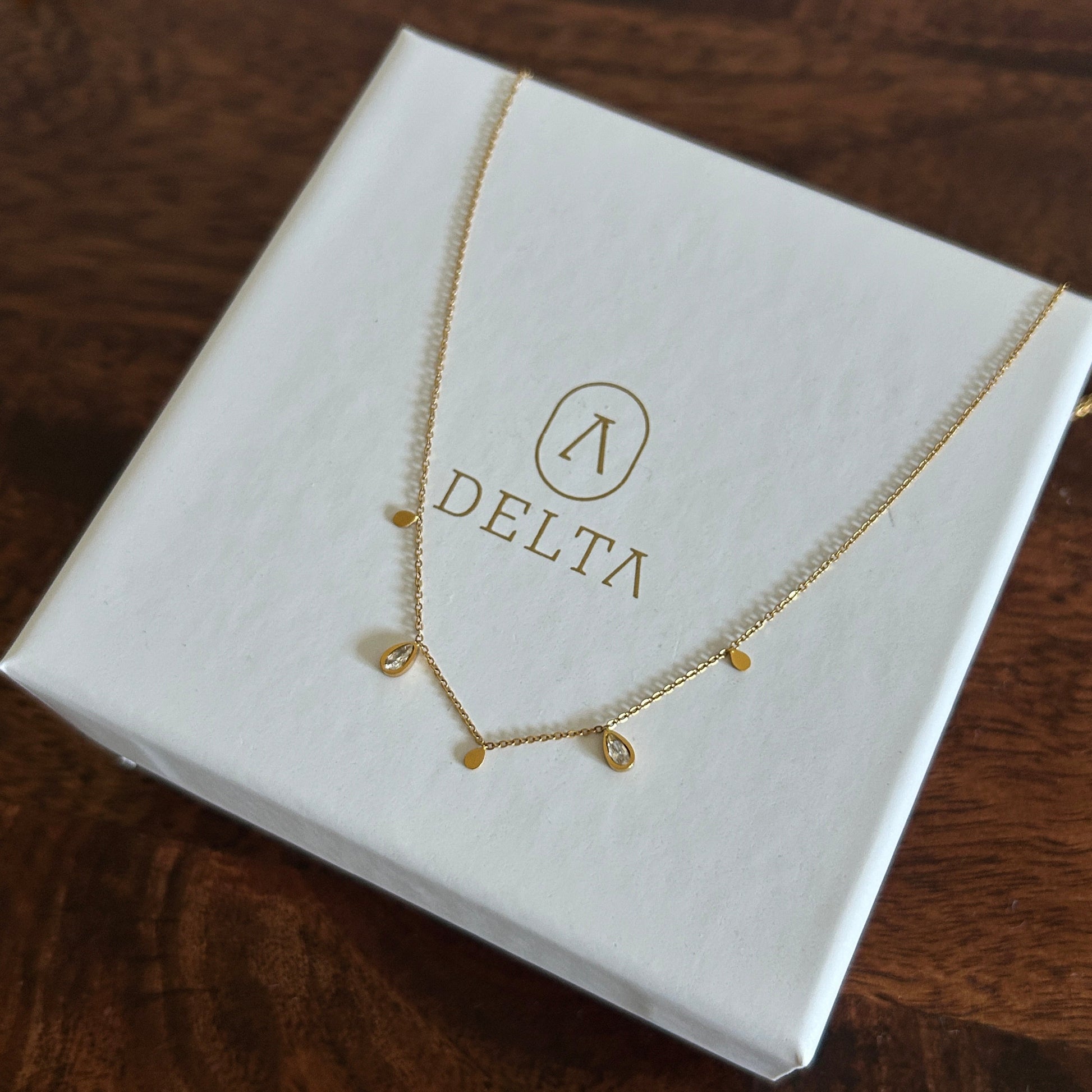 Gold necklace on a white box with 'DELTA' branding on a wooden surface