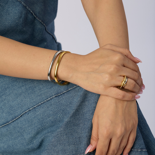 Close-up of a person's hands wearing gold bracelets and rings on a denim background