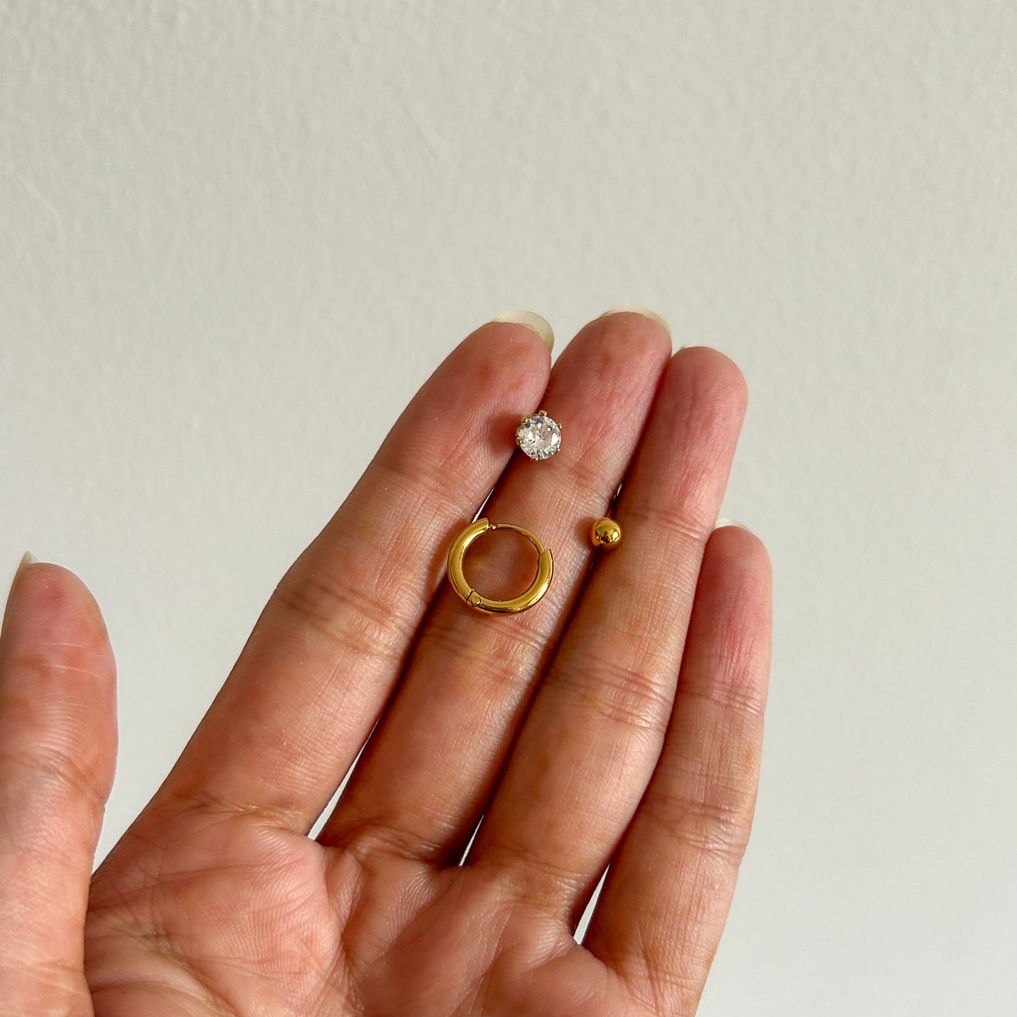Hand holding two gold rings with a clear stone against a plain background