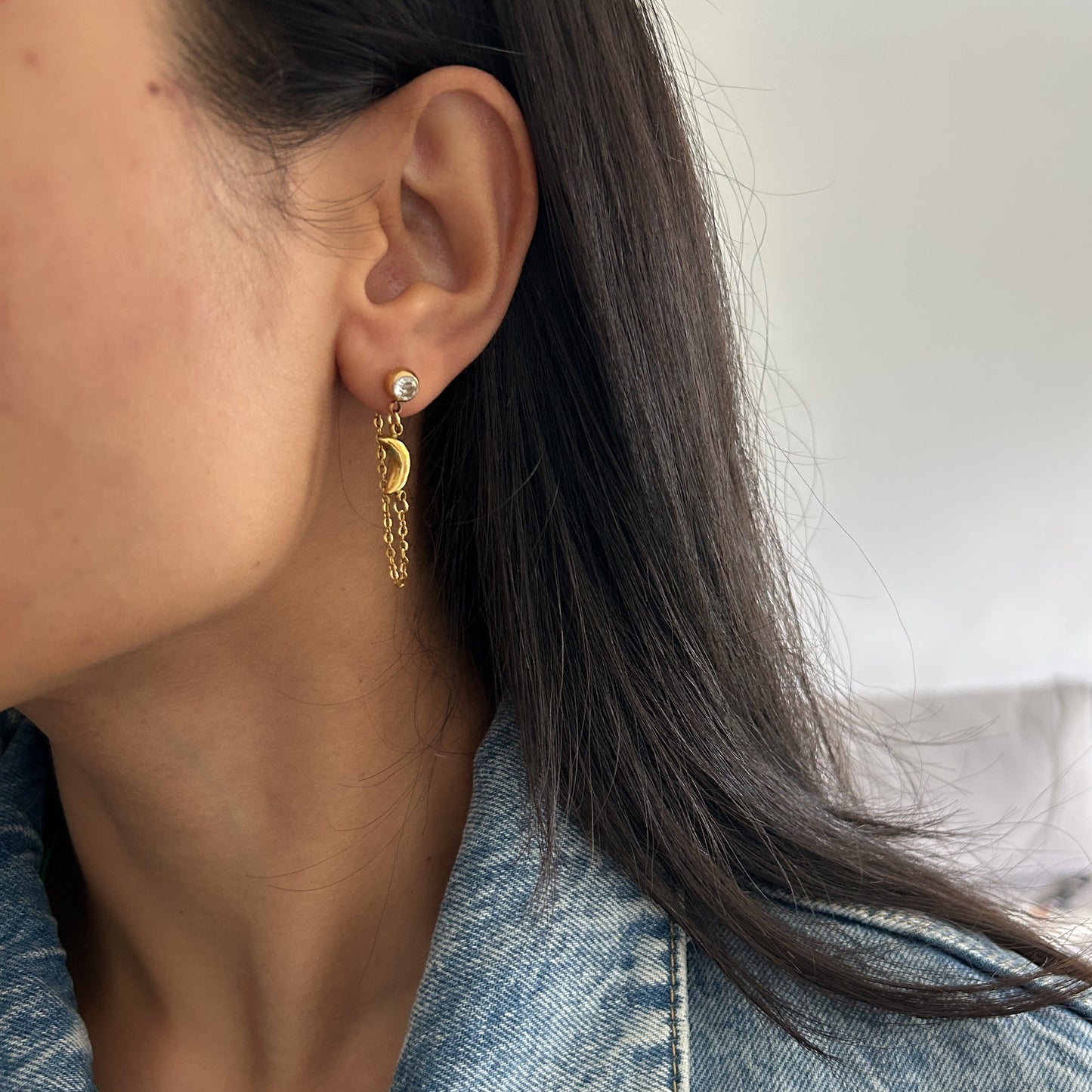 Close-up of a person wearing gold hoop earrings with a denim jacket.
