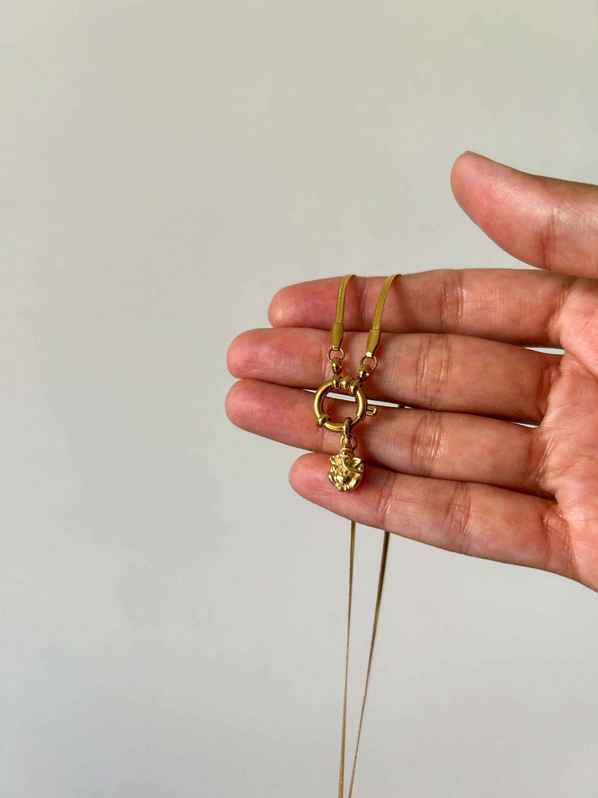 Gold necklace held in a hand against a plain background