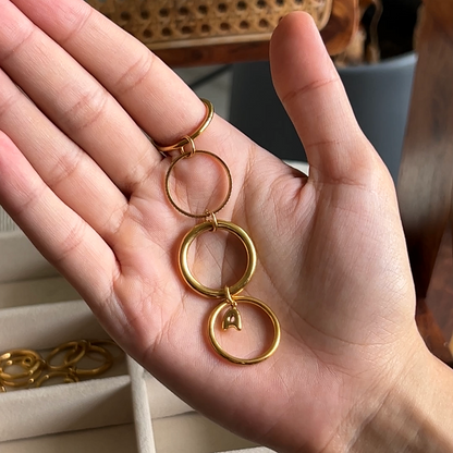 A close-up of a hand holding a gold keychain with three interlocking circular rings, with a blurred indoor background and a phone app interface visible around the edges.