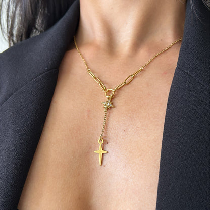Gold necklace with a cross pendant on a person wearing a dark blazer.
