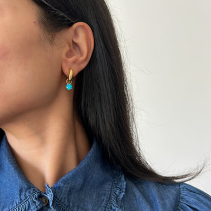 Close-up of a person wearing gold earrings with a blue gemstone against a white background