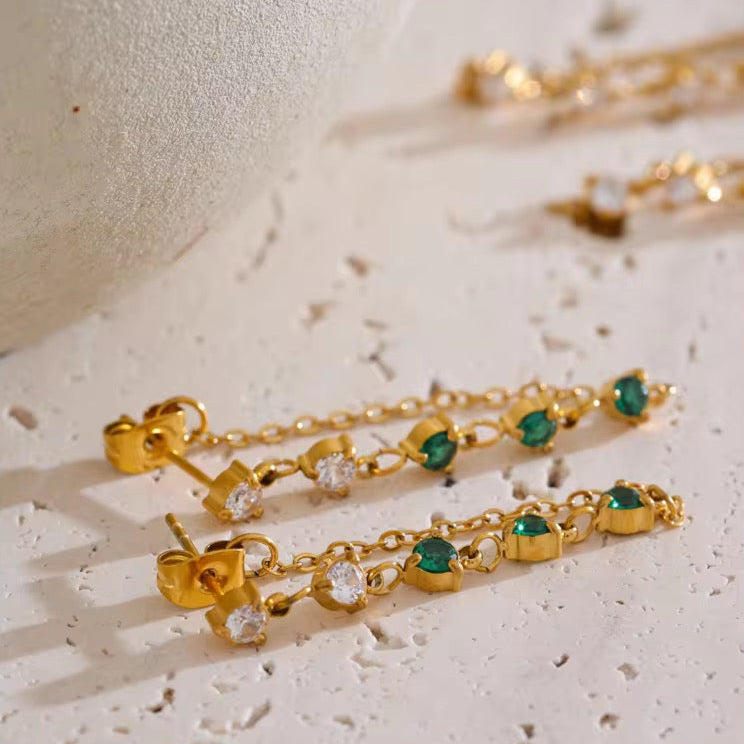 Gold earrings with green gemstones on a textured surface