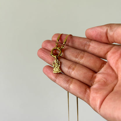Gold necklace with a pendant held in a hand against a plain background
