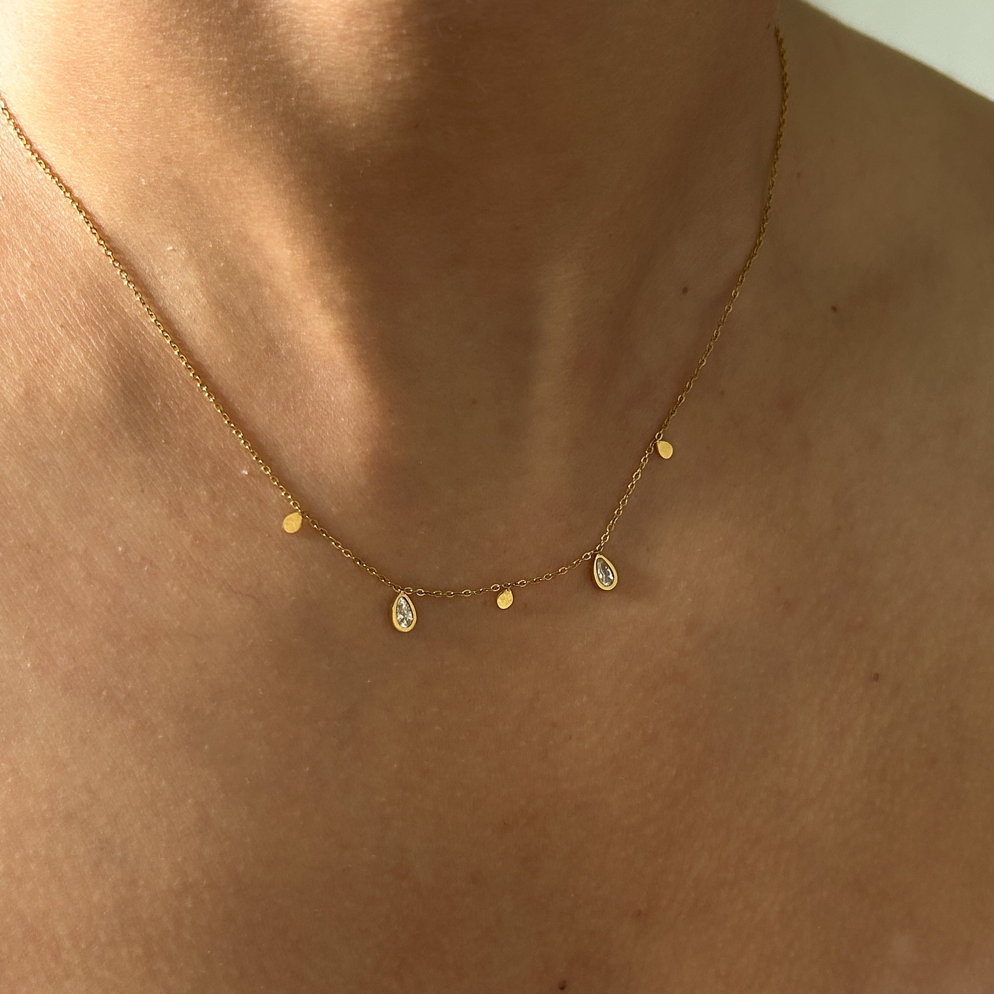 Gold necklace with teardrop-shaped pendants on a person's neck