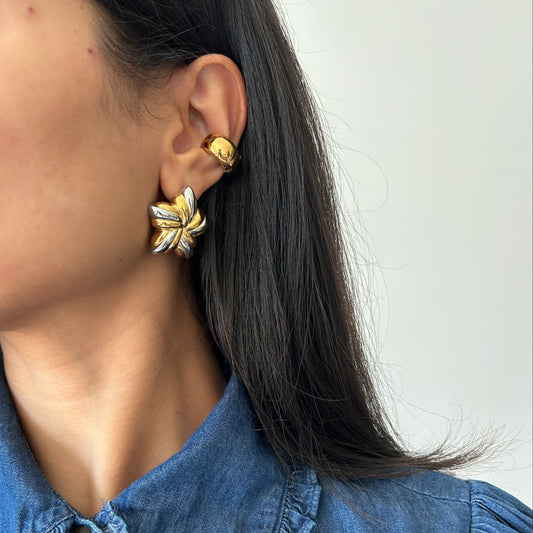 Close-up of a person wearing gold leaf earrings with a plain background
