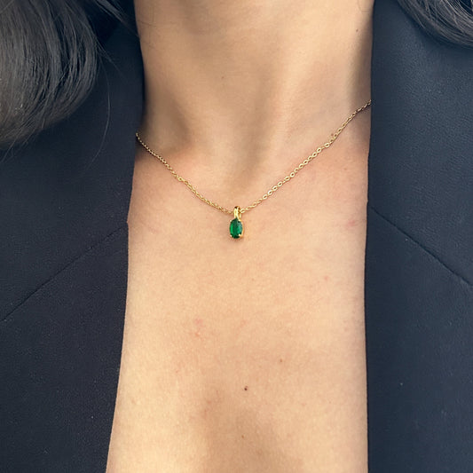 Gold necklace with a green gemstone pendant on a person's neck against a dark background