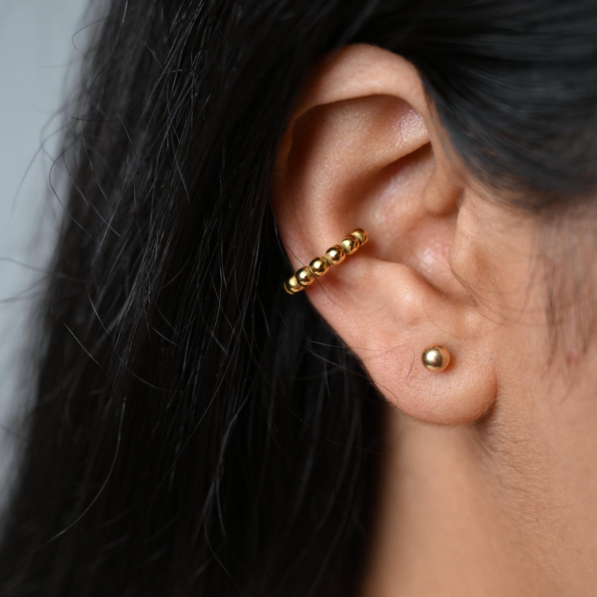 Close-up of a gold beaded earcuff wrapped around the ear, showcasing its subtle design and polished finish. Worn without a piercing.
