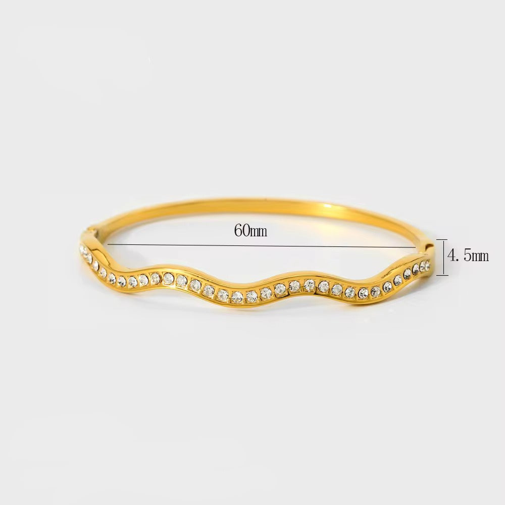 Gold bracelet with wavy design and embedded stones on a white background