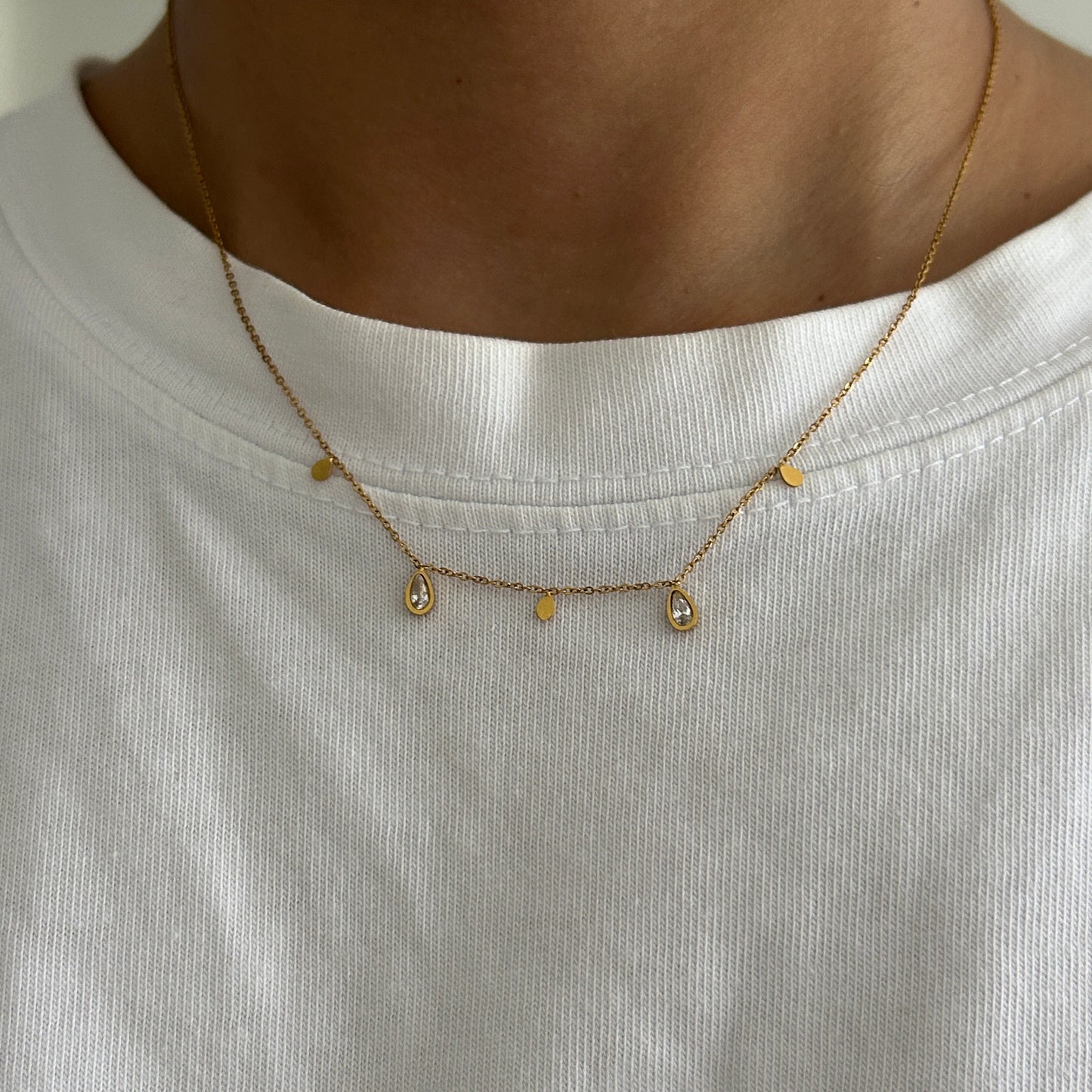 Close-up of a gold necklace with small beads on a white shirt.