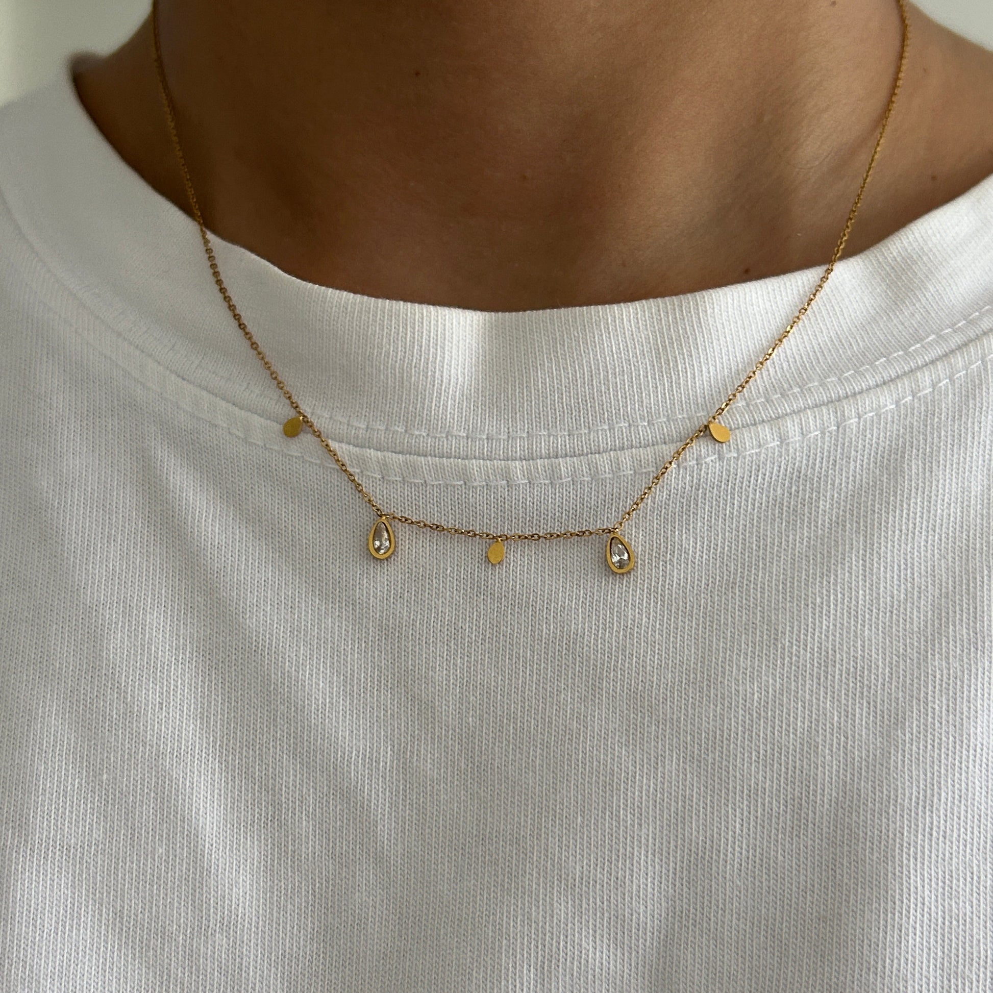 Close-up of a gold necklace with small beads on a white shirt.
