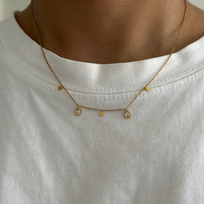 Close-up of a gold necklace with small beads on a white shirt.
