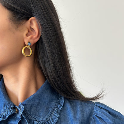Person wearing gold hoop earrings with a blue top against a white background