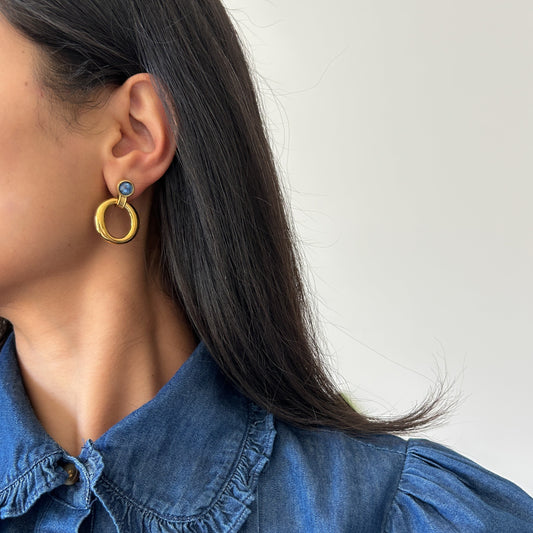 Person wearing gold hoop earrings with a blue top against a white background