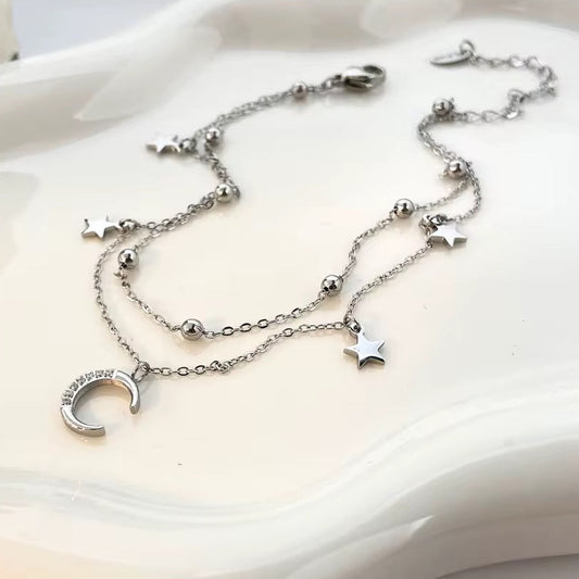 Silver anklet with star and moon charms on a white dish