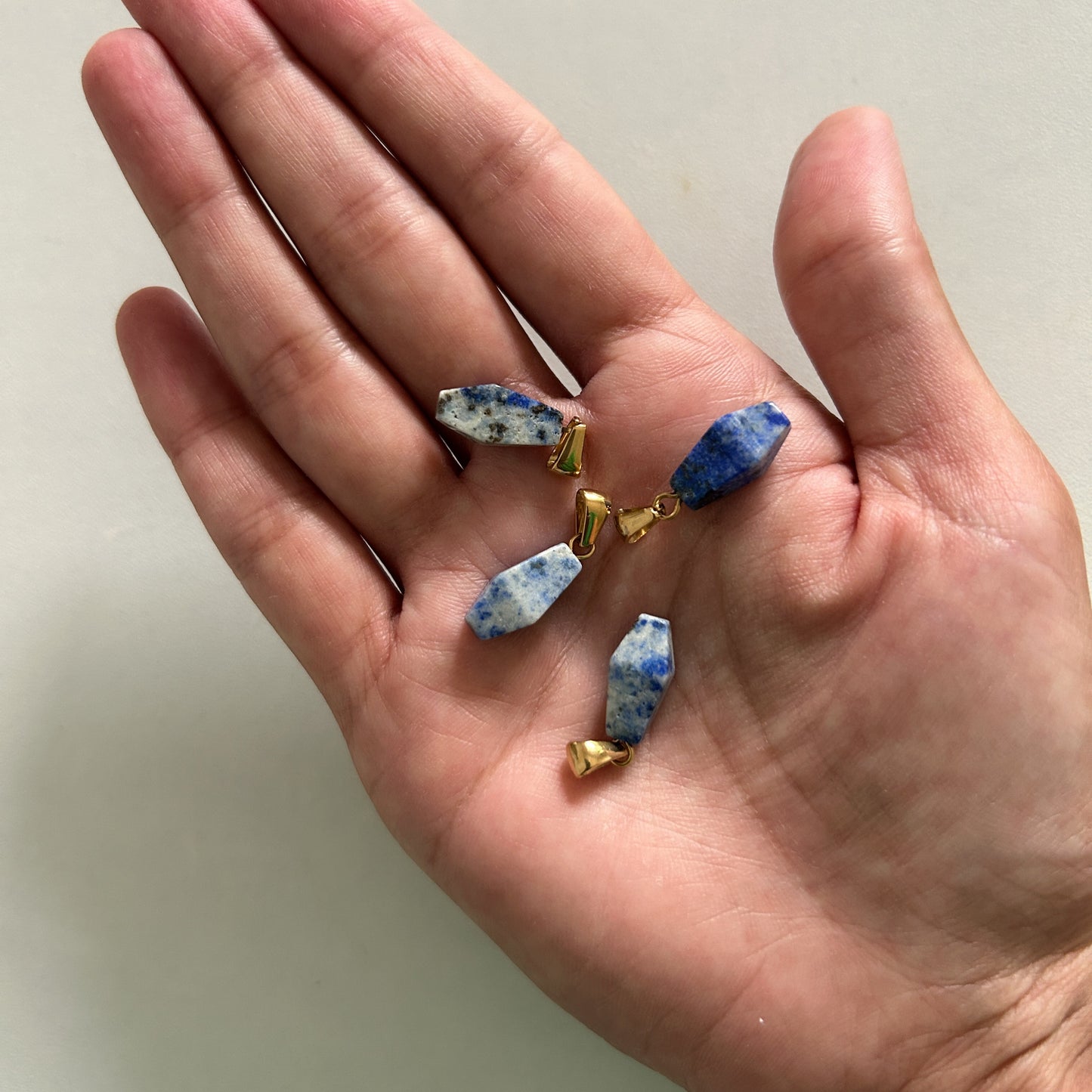 Hand holding three small blue and gold lapis lazuli charms  against a plain background