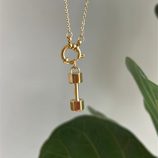 Gold necklace with a dumbbell pendant on a light background